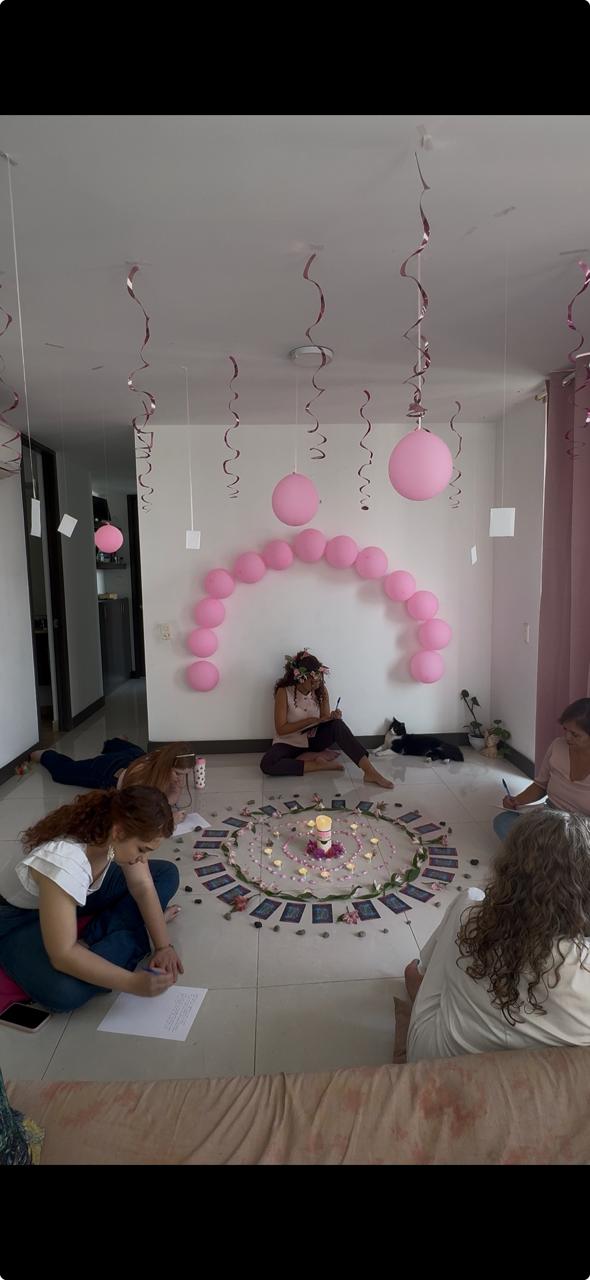 Encuentro de cumpleaños con globos rosados y participantes escribiendo alrededor del altar